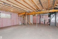 Unfinished basement offering expansive concrete flooring, exposed ceiling joists, framed walls with pink insulation, and a basement window - 