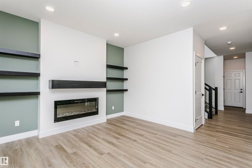 Modern living area featuring a built-in electric fireplace with a black mantel, recessed lighting, and wood-finish flooring - 6210 Dansereau Crescent, Beaumont, AB 