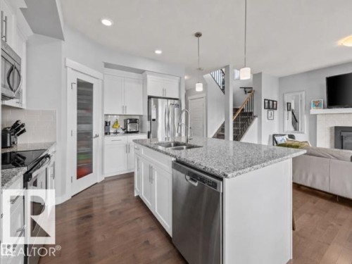 Kitchen featuring a central island with granite countertops, stainless steel appliances, white cabinetry, wood-finish flooring, and a glass-paneled pantry door - 607 40 Street, Edmonton, AB 