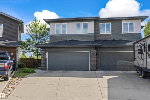 Modern duplex exterior featuring multi-toned horizontal siding, dark asphalt shingles, and two integrated single-car garages with dark panel doors - 607 40 Street, Edmonton, AB 