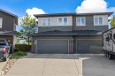 Modern duplex exterior featuring multi-toned horizontal siding, dark asphalt shingles, and two integrated single-car garages with dark panel doors - 607 40 Street, Edmonton, AB 