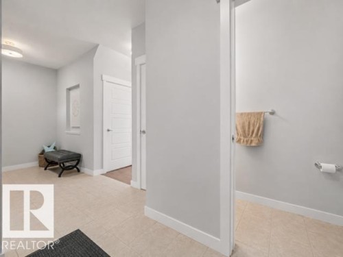 Hallway featuring light neutral wall paint, tile flooring, white baseboards, and a contemporary flush-mount ceiling light fixture - 607 40 Street, Edmonton, AB 