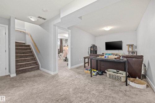 Carpeted lower level featuring light gray walls, white trim, and a staircase with a wood handrail - 607 40 Street, Edmonton, AB 