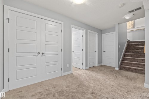 Spacious carpeted area featuring modern five-panel doors, neutral gray wall paint, and a carpeted staircase with a wood handrail - 607 40 Street, Edmonton, AB 