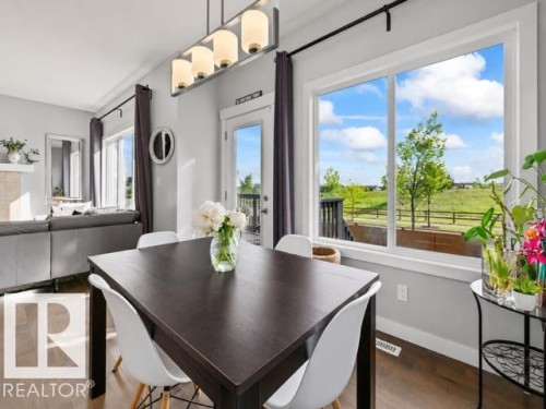 Open concept dining area featuring wood-finish flooring, an overhead linear light fixture, a large window, a glass-paned door, and a light-toned wall color - 607 40 Street, Edmonton, AB 