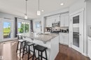 Modern kitchen featuring a large central island with seating, white shaker cabinetry, stainless steel appliances, and wood-finish flooring - 607 40 Street, Edmonton, AB 