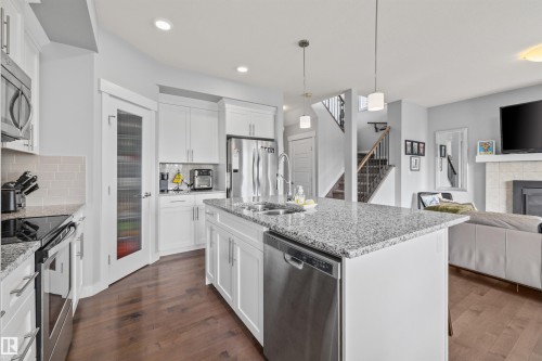 Modern kitchen featuring an expansive center island with a dual-basin sink, stainless steel appliances, white cabinetry, wood-finish flooring, and a walk-in pantry with a frosted glass door - 607 40 Street, Edmonton, AB 