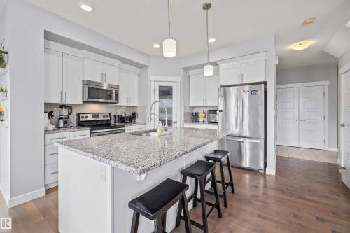 Modern kitchen featuring white cabinetry, stainless steel appliances, granite countertops, and wood-finish flooring - 607 40 Street, Edmonton, AB 