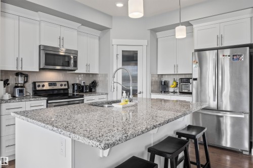 Kitchen featuring a central island with a speckled countertop, white cabinetry, stainless steel appliances, pendant lighting, and a glass-paneled door - 607 40 Street, Edmonton, AB 