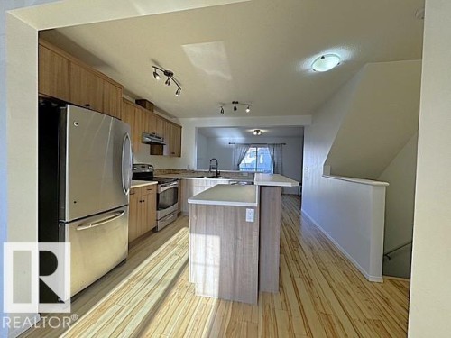 Open-concept kitchen featuring wood-finish flooring, stainless steel appliances, track lighting, and a breakfast bar island - #13 3751 12 Street, Edmonton, AB 