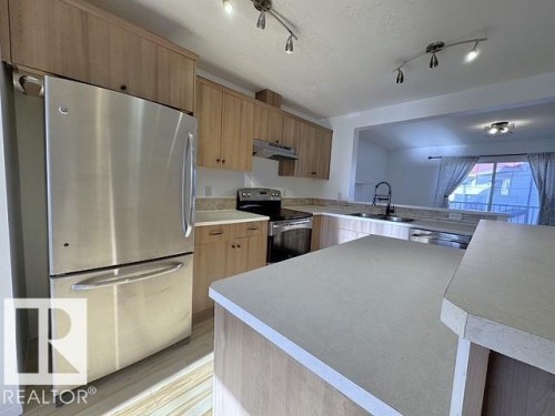 Modern kitchen featuring light wood-finish cabinetry, stainless steel appliances, light-toned countertops, and track lighting - #13 3751 12 Street, Edmonton, AB 