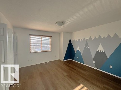 Interior room featuring wood-finish flooring, a white ceiling with a flush-mount light fixture, and a window with horizontal blinds - #13 3751 12 Street, Edmonton, AB 