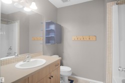 Bathroom featuring a vanity with a white sink, a mirror with overhead lighting, a wall-mounted storage cabinet, and a shower with tiled walls - 