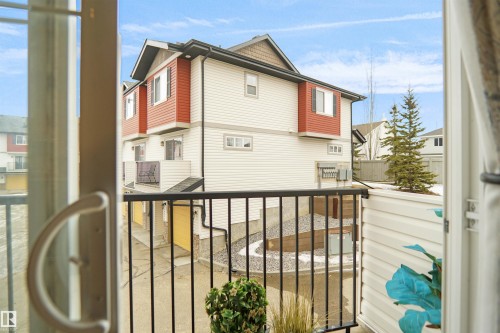 This property features durable vinyl siding, a private balcony with black railings, and an exterior highlighted by a combination of white and red paneling - #13 3751 12 Street, Edmonton, AB 