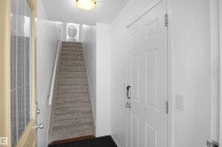 Entryway featuring a white paneled door with a modern handle, a carpeted staircase with white railings, and a ceiling-mounted light fixture - 