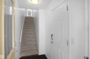 Entryway featuring a white paneled door with a modern handle, a carpeted staircase with white railings, and a ceiling-mounted light fixture - #13 3751 12 Street, Edmonton, AB 