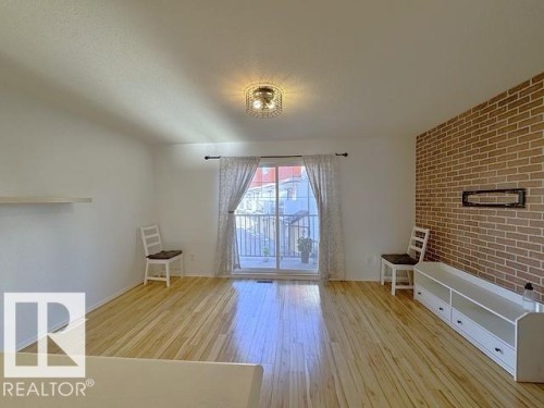 Living area featuring wood-finish flooring, a full-wall brick-pattern accent, and a built-in media console - #13 3751 12 Street, Edmonton, AB 