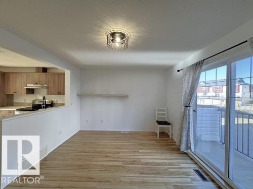 Open-concept living area featuring wood-finish flooring, a contemporary wire cage flush mount light fixture, and a sliding glass door providing abundant natural light - #13 3751 12 Street, Edmonton, AB 