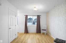 The property features light-toned hardwood flooring, a window with curtains, and a wall adorned with patterned wallpaper - 