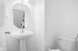 Bathroom featuring a white pedestal sink with a chrome faucet, an oval mirror, and a white toilet - 