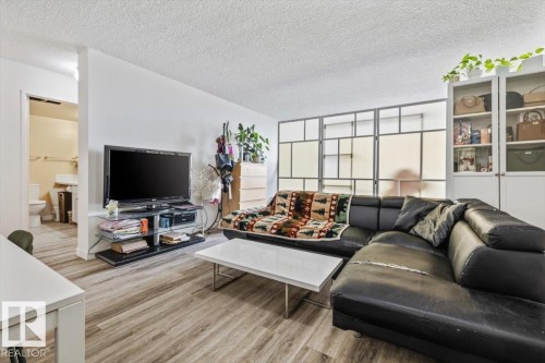 Open-concept living area featuring wood-finish flooring, white walls, and a textured ceiling - 77 8735 165 Street, Edmonton, AB 