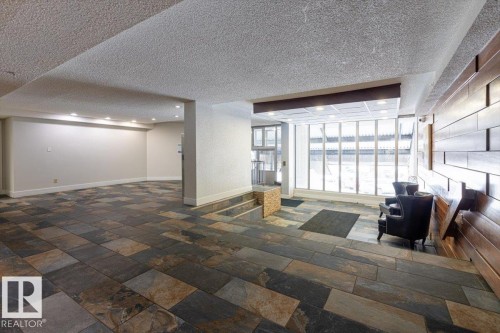 Spacious common area featuring multi-toned slate tile flooring, recessed ceiling lighting, a prominent wood accent wall, and expansive floor-to-ceiling windows - 77 8735 165 Street, Edmonton, AB 