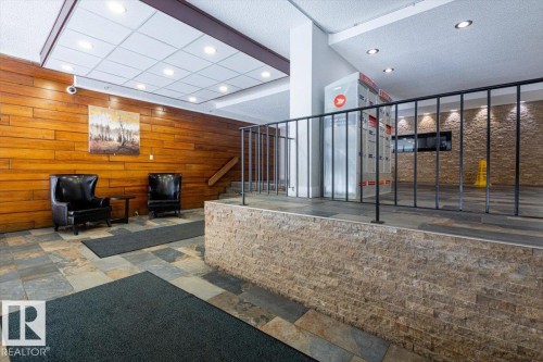 Entryway featuring multi-toned slate flooring, a wood-paneled accent wall, recessed ceiling lighting, a stone veneer half-wall, and a black metal railing - 77 8735 165 Street, Edmonton, AB 