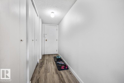 Hallway featuring wood-finish flooring, a white entry door with security hardware, and multiple white closet doors - 77 8735 165 Street, Edmonton, AB 