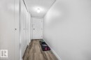 Hallway featuring wood-finish flooring, a white entry door with security hardware, and multiple white closet doors - 77 8735 165 Street, Edmonton, AB 