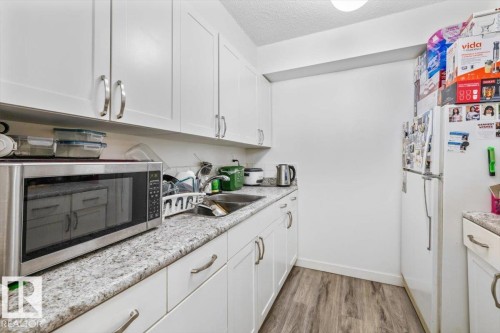 White cabinetry with brushed nickel hardware, granite-look countertops, stainless steel sink, and wood-finish flooring - 77 8735 165 Street, Edmonton, AB 