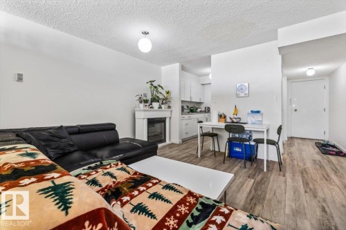 Living area featuring wood-finish flooring, a white fireplace surround with an insert, and a kitchen area with white cabinetry - 77 8735 165 Street, Edmonton, AB 