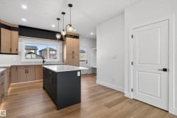 Contemporary kitchen featuring a central island with a light-toned countertop, wood-finish flooring, recessed lighting, modern pendant light fixtures, and a white tile backsplash - 