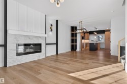 Open-concept living space featuring wood-finish flooring, a contemporary fireplace with a stone surround, and a kitchen with an island and pendant lighting - 