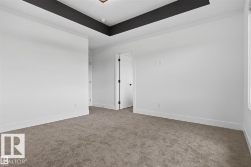 Spacious interior room featuring a tray ceiling with dark accent, light-colored walls, neutral carpeting, and white trim - 41 River Birch Way, St. Albert, AB 