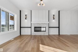 Spacious interior featuring a contemporary fireplace with a light-toned surround, wood-finish flooring, white walls, and a multi-pane window - 