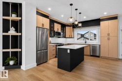 Modern kitchen featuring light wood-finish cabinetry and a contrasting black island with a white countertop - 