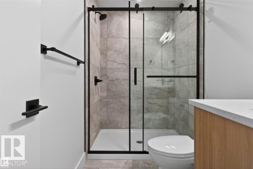 Modern bathroom featuring a glass-enclosed shower with matte black fixtures, large format tile walls, and a wood-finish vanity with a light-toned countertop - 41 River Birch Way, St. Albert, AB 