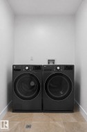 Dedicated laundry area featuring a front-loading washer and dryer set, neutral wall paint, and natural stone-look floor tiles - 