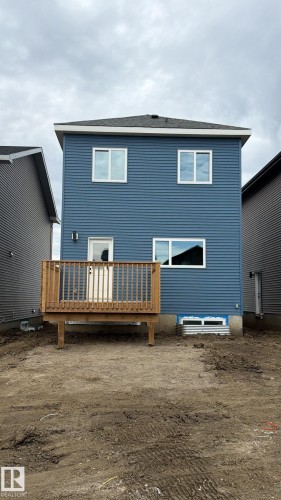 Rear exterior featuring blue horizontal siding, white trim, a dark asphalt shingle roof, a wooden deck, and white framed windows - 41 River Birch Way, St. Albert, AB 