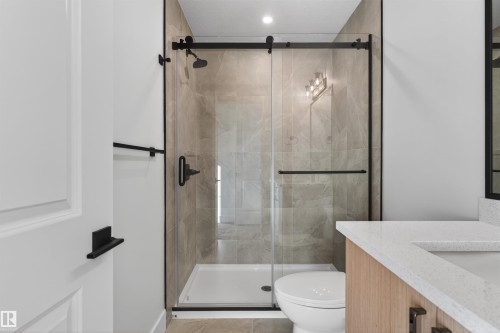 Modern bathroom featuring a glass-enclosed shower with matte black hardware, floor-to-ceiling tiled shower walls, a white shower pan, and a contemporary vanity with a light wood-finish and white countertop - 41 River Birch Way, St. Albert, AB - Indoor Photo Showing Bathroom