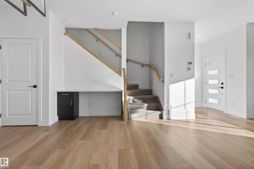 Open-concept entryway featuring light wood-finish flooring, a contemporary front door with horizontal lites, and a carpeted staircase with wood handrails - 41 River Birch Way, St. Albert, AB - Indoor Photo Showing Other Room