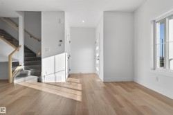 Bright entryway featuring wood-finish flooring, a modern staircase with glass railing and wood handrails, and a white paneled door with frosted glass inserts - 