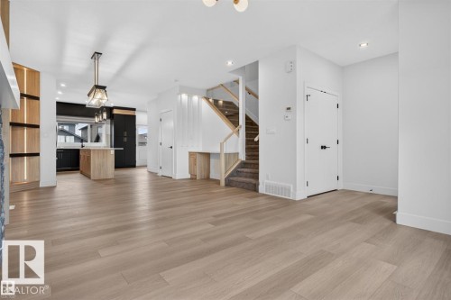 Open-concept living space featuring wide plank wood-finish flooring, a modern kitchen with a central island, contemporary pendant lighting, a built-in desk area under the staircase, and a stone-clad fireplace surround - 41 River Birch Way, St. Albert, AB 