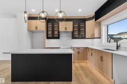 Kitchen featuring a central island with white countertop, light wood-finish cabinetry, black accent cabinetry with glass panels, white subway tile backsplash, and wood-finish flooring - 