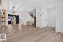 Open-concept living space featuring wide plank wood-finish flooring, a modern kitchen with a central island, contemporary pendant lighting, a built-in desk area under the staircase, and a stone-clad fireplace surround - 41 River Birch Way, St. Albert, AB 