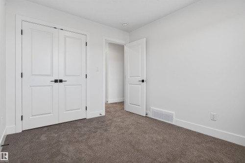 Neutral-toned carpeted room featuring white walls, white baseboards, and a white six-panel bifold closet door with matte black hardware - 41 River Birch Way, St. Albert, AB - Indoor Photo Showing Other Room