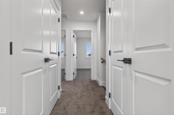 Hallway featuring neutral-toned carpet flooring, white paneled doors, and matte black hardware - 