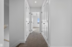 Hallway with carpet flooring, white walls, and multiple paneled doors with black hardware - 