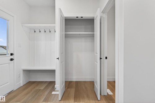 Entryway featuring built-in bench seating and coat hooks, wood-finish flooring, a white paneled door with window, and a spacious closet with double doors - 41 River Birch Way, St. Albert, AB - Indoor