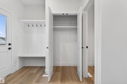 Entryway featuring built-in bench seating and coat hooks, wood-finish flooring, a white paneled door with window, and a spacious closet with double doors - 